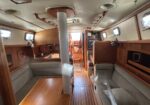 Wood-paneled yacht interior with L-shaped gray sofas, a central wooden table, and a gray pillar in the middle.