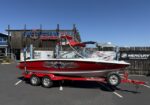Red and gray speedboat on a red trailer parked in a lot outside a boat services shop named Pacific Boat Services.
