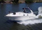 White speedboat with blue canopy speeding on a river, creating a large wake
