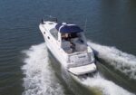 A white motorboat speeding through open water, creating a frothy wake behind it, viewed from above with a blue canopy over the seating area