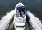 Aerial view of a white motorboat with a blue canopy cruising through dark water, creating a large wake on both sides.