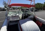 Open-top speedboat interior with white and red upholstery, two front seats and a steering cockpit, wakeboard racks on the sides, parked in a lot.