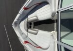 Top-down view of a white speedboat bow, with cushioned gray seats and built-in cup holders, parked on pavement. Red accents adorn the sides.
