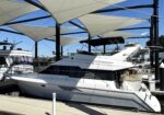 Large white luxury yacht docked at a marina with overhead fabric shade sails and blue sky above.