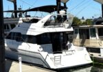 White motor yacht docked at a marina under a covered structure, with other boats and blue sky in the background.