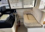 Cockpit of a boat with a steering wheel, navigation instruments, and a beige captain's seat by window blinds.