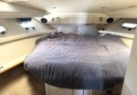 Cozy cabin bedroom with a full bed, gray duvet, and beige walls featuring porthole windows and built-in storage drawers below the bed.