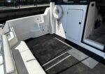 White boat cockpit with cushioned seating, a coiled rope on the wall, and built-in storage hatch nearby on a sunny dockside scene