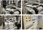 Industrial engine compartment with a large white engine, metal pipes and hoses surrounding it.