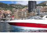 White and red motor yacht docked by a Mediterranean-style city, a woman in a red dress on the deck with hillside buildings in the background