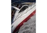 People stand on a white and red motorboat cutting through chop in the water, spray trailing behind them