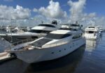 Large white luxury motor yacht docked at a marina with other boats and a blue, cloudy sky above.