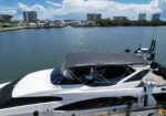 White motor yacht docked at a marina with calm water and waterfront houses in the background across the canal.