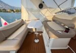 Cockpit seating area on a luxury boat with beige cushioned benches, a white pedestal table, and teak decking.