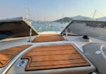 View from a luxury boat deck with teak panels, open sunroofs, and a calm harbor with moored sailboats and distant hills.