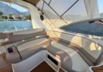 Yacht deck seating with tan cushions and a wood floor; water, coastline, and mountains visible in the background