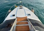 Top-down view of a white speedboat bow cruising on blue water, teak steps leading to the cockpit, stainless rails on sides.