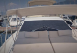 Luxury motor yacht deck with cream sun loungers, cushions, and a shaded canopy at a marina.
