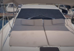 Beige cushioned sun beds on the deck of a white yacht, with a windshield and canopy overhead.