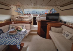Luxurious yacht salon with cream upholstery, wooden cabinetry, a chevron table with flowers, and a wall-mounted TV.