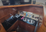 Small boat galley with wooden cabinets, black countertop, double sink, stove, and various cookware and bottles along the counter.