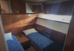 Twin bunk beds in a small wooden cabin, blue patterned bedspreads and white pillows, with built-in shelves above.