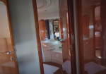 Inside a yacht cabin: wood-paneled doors, curved white sink area, and a mirror reflecting a bed.
