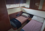 Boat cabin with two single beds, striped bedding, wood paneling, and a small nightstand between them.
