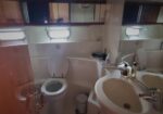 Small bathroom with a toilet and sink, porthole windows, and mirrored cabinets above the sink area on a compact boat interior.