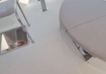 White boat deck showing an open hatch on the left, metal railing, and a rounded cushioned seat on the right.