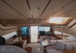 Luxurious yacht cabin living area with beige sofas, wooden shelves, and a small coffee table with flowers; deck door at the back letting in light.