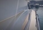 Close-up of a white yacht hull at a marina, with rails and calm water in the background.