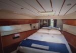 Cozy yacht cabin with a double bed, white and blue bedding, a folded towel at the foot, and wood-paneled storage along the sides.