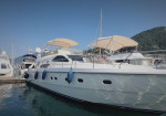 White luxury motor yacht docked at a sunny marina, with beige canvas covers and blue fenders along the hull.