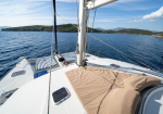 Sailboat deck with beige sun loungers, striped towels, and open cockpit overlooking calm blue sea and distant green islands.