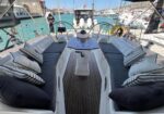 Luxurious sailboat cockpit with two long cushioned benches, striped pillows, a central table, and marina in the background.