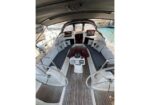 Twin steering wheels in a sailboat cockpit with cushioned benches and a wooden central table; navigational instruments and compass at the helm.