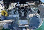 Back view of a cruising sailboat cockpit with twin steering wheels and a stern swim platform under a bimini top, ladder folded at the edge.