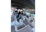 Spacious sailboat cockpit with twin steering wheels, teak decking, and cushioned seating under a canopy near calm water.
