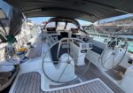 Sailboat cockpit with two steering wheels, a wood deck, and cushioned seating under a canopy at a marina.