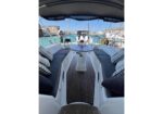 Open cockpit of a luxury sailing yacht with gray cushioned benches and a central pedestal table, marina in the background.