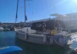 White sailing yacht docked at a sunny marina with fenders along the hull and cockpit cover in place