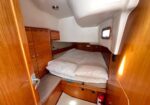 Wood-paneled sleeping cabin with a double bed, storage cabinets, and a small porthole window.