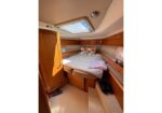 Wood-paneled boat cabin with a centered V-shaped bed, pillows with starfish patterns, and a skylight overhead.