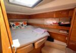 Yacht cabin with a double bed, nautical shell pillows, and built-in wooden storage along the walls.