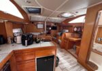 Wooden boat galley and navigation area with countertop appliances and seating, showing a sink and solar panels on the ceiling.