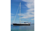 Sailboat with black hull and white deck anchored on calm blue water under a clear sky, American flag at stern