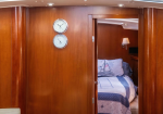 Wood-paneled cabin with two round clocks on the wall, view into a neatly made bed with a sailboat quilt.