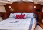 Cozy yacht cabin bed with nautical quilt, sailboat pillows, and a red anchor throw pillow against polished wood walls.