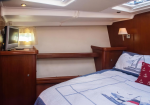 Wood-finished yacht cabin with a bed, wall lamp, TV on a cabinet, and a ship-themed quilt.